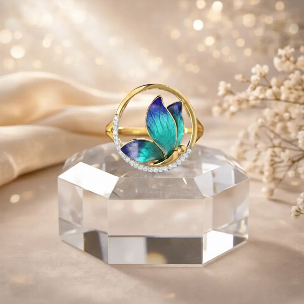 Gold ring with blue and green leaf design on a crystal stand with a soft background