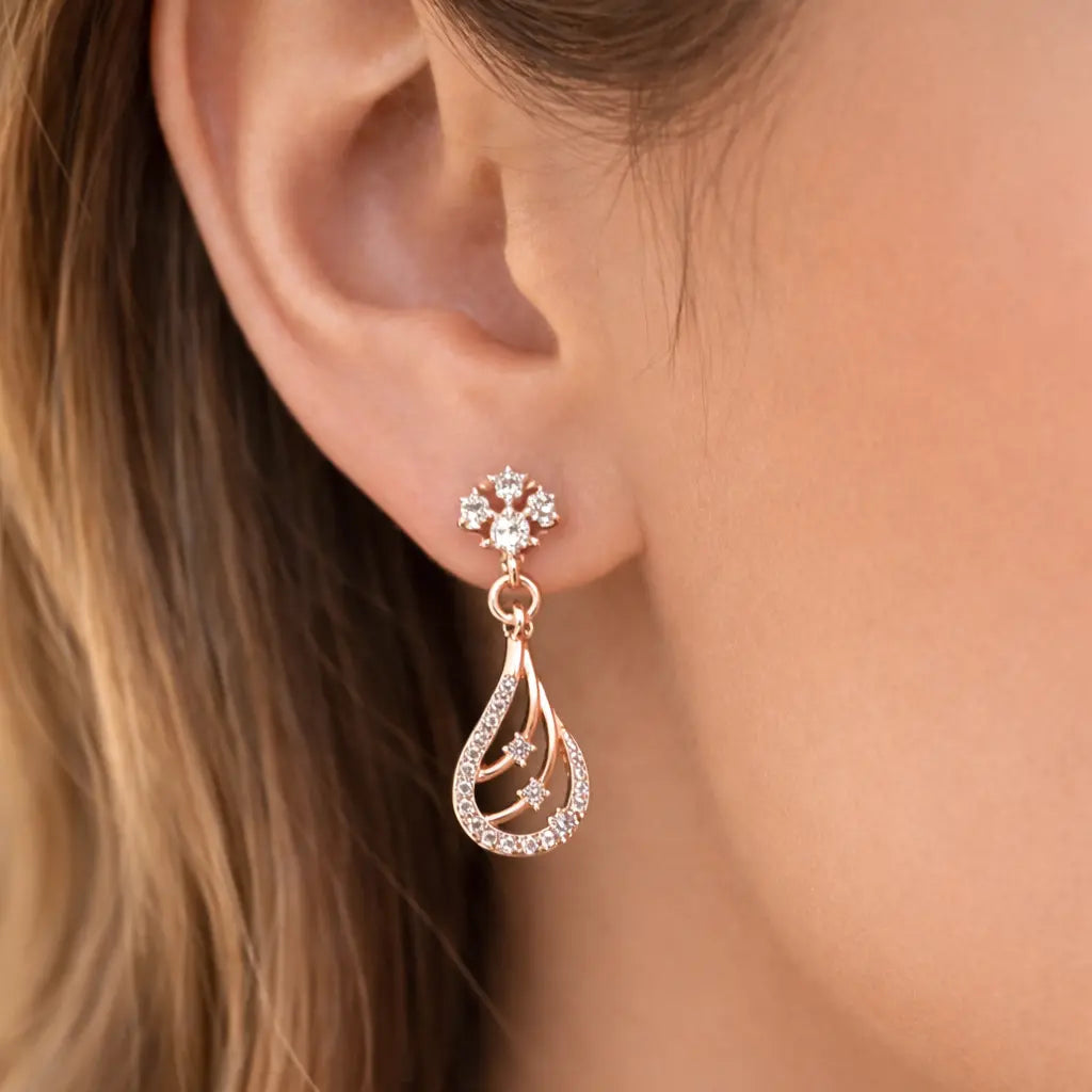Close-up of a woman wearing a rose gold teardrop earring with a snowflake design.