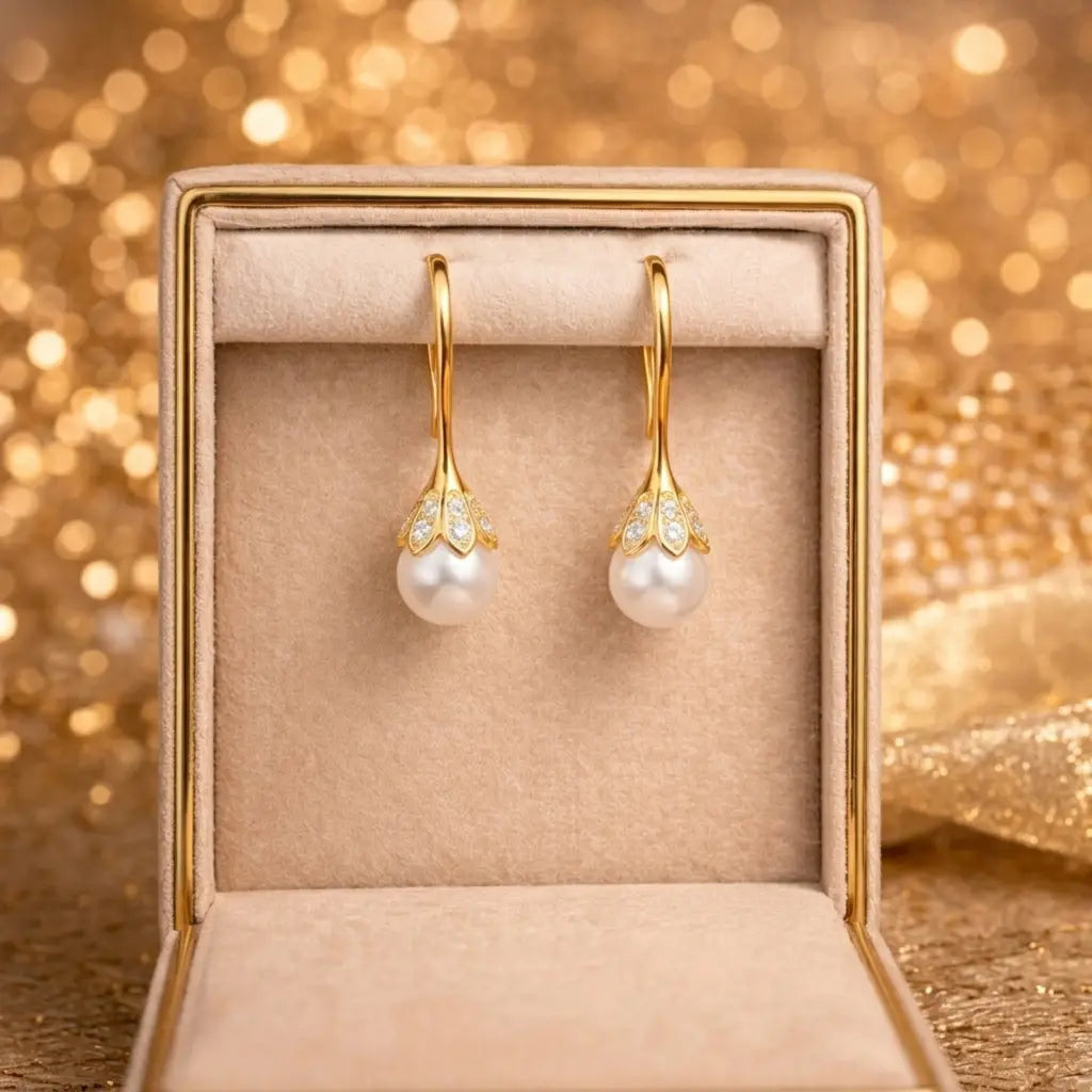 Gold earrings with pearls in a jewelry box against a glittering gold background