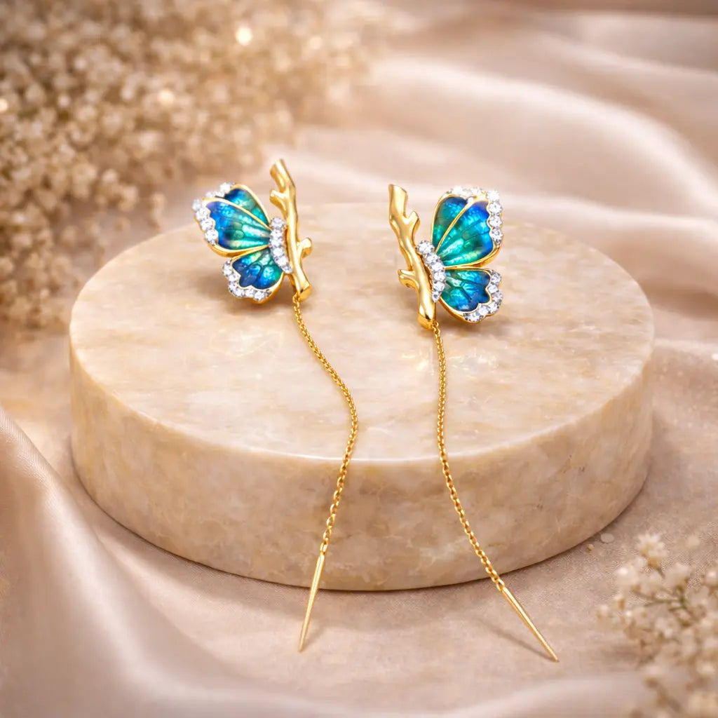 Butterfly-shaped earrings with gold and blue design on a beige stone surface.