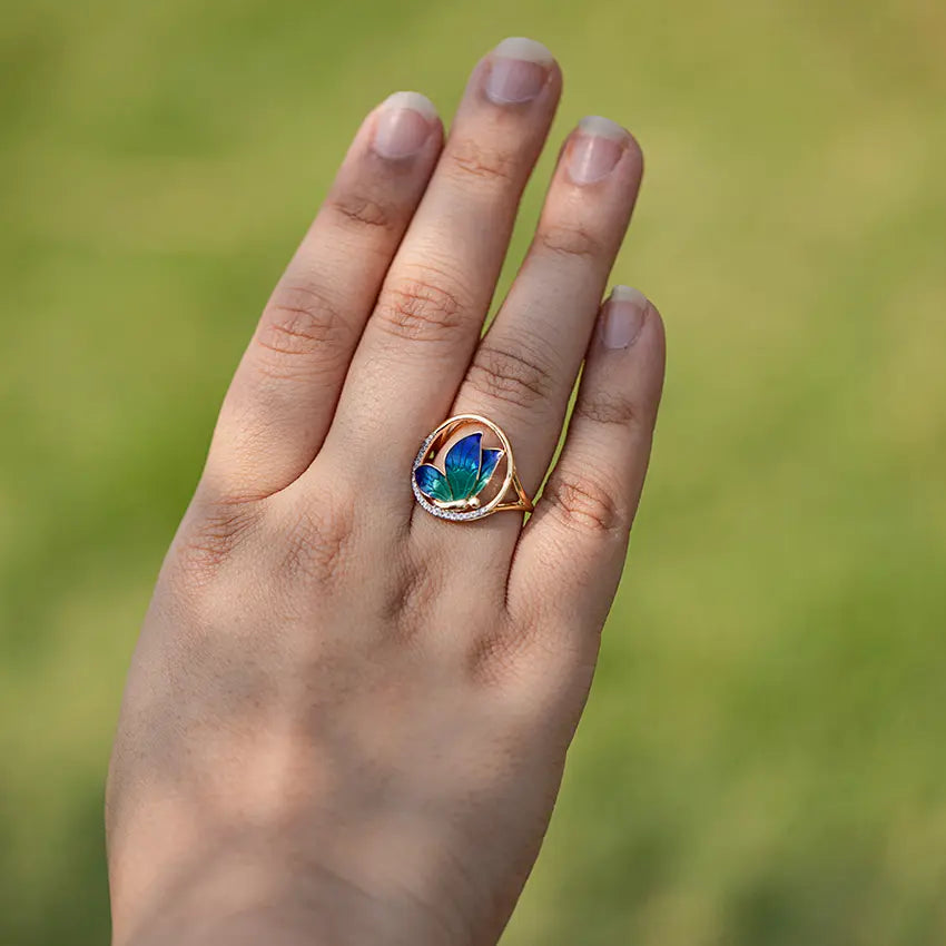 Hand wearing a ring with a colorful gemstone against a blurred green background