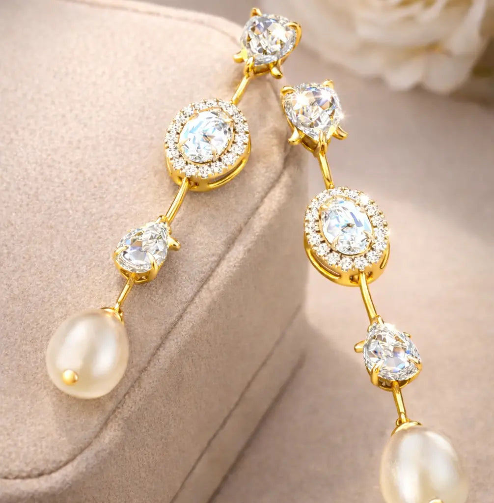 Gold earrings with pearls and clear gemstones on a beige surface