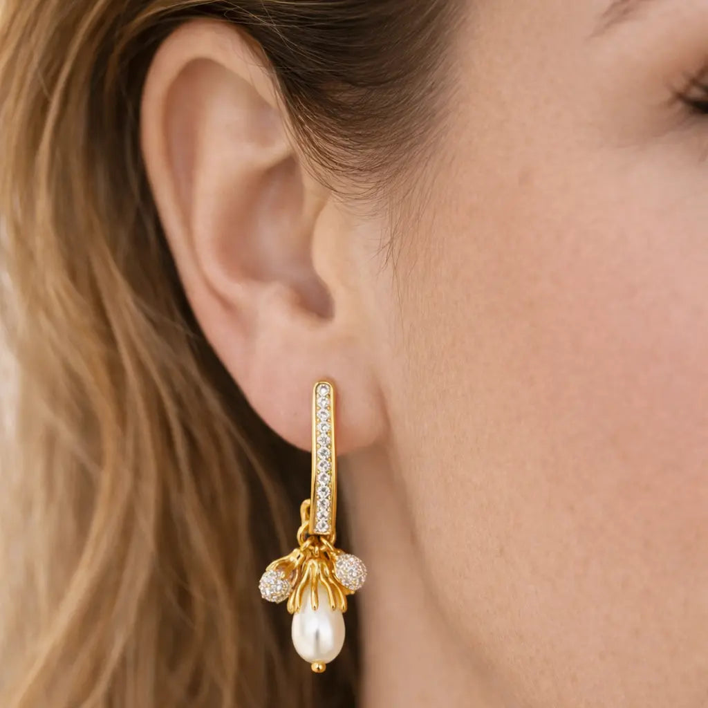 Gold earring with a pearl drop worn by a person