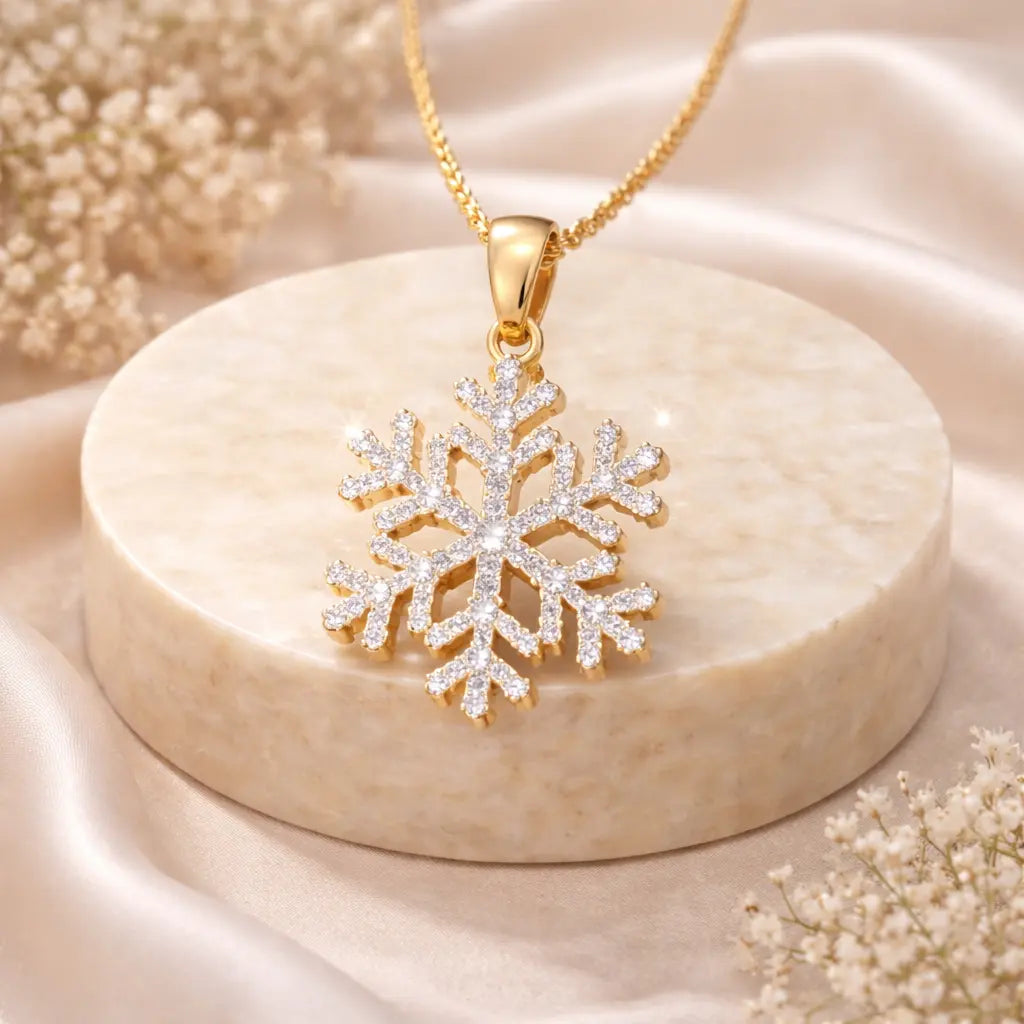 Gold snowflake pendant necklace on a beige stone surface with dried flowers.