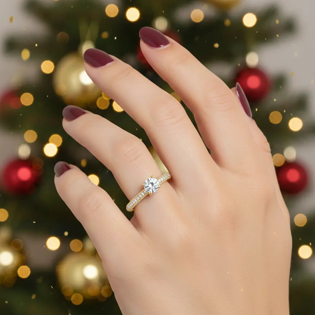 Hand wearing a diamond ring with a blurred Christmas tree background