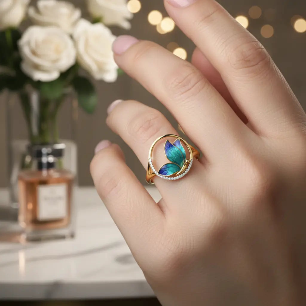 Hand wearing a colorful ring with a blurred background of flowers and perfume bottle.