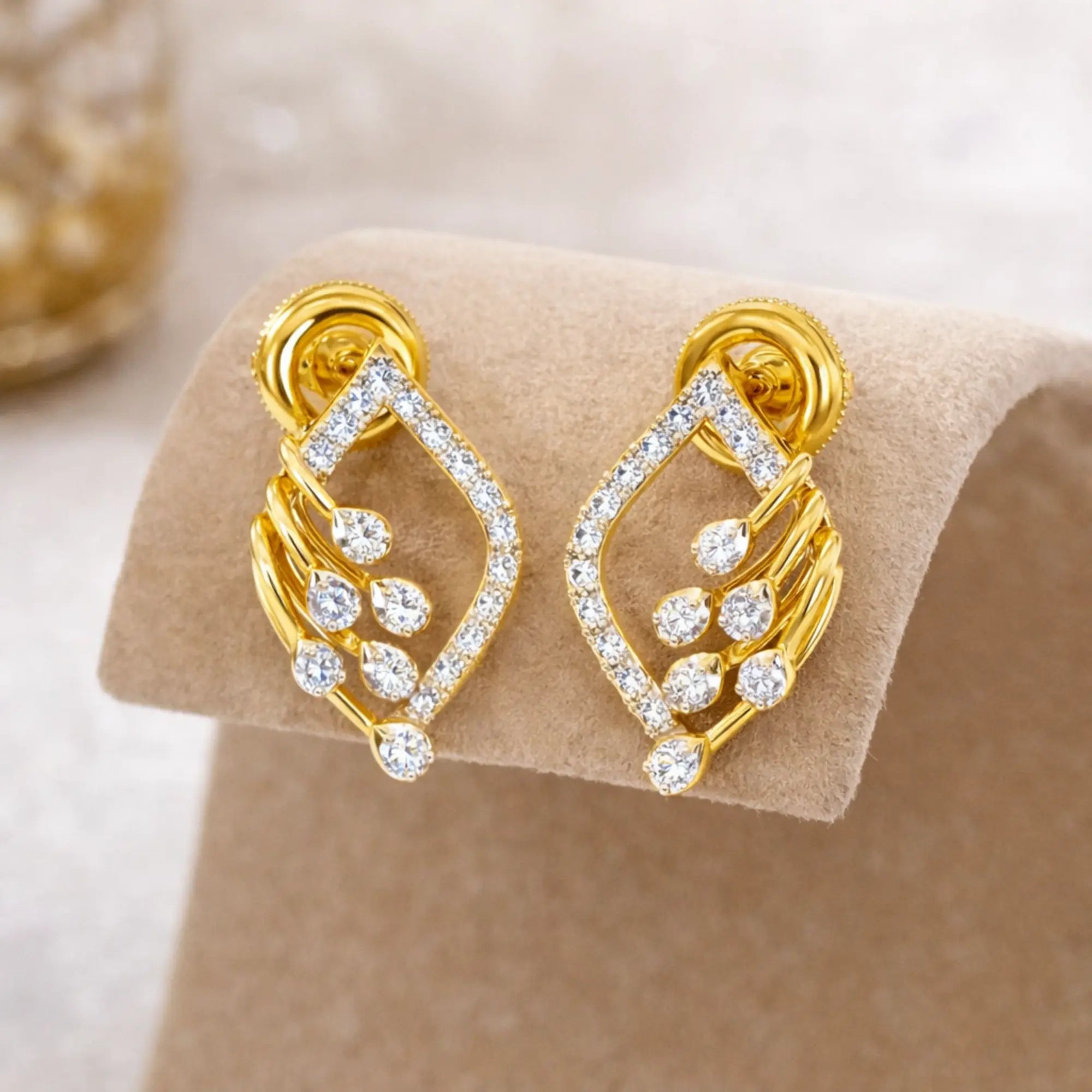 Gold earrings with diamond-like stones on a beige stand